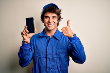 Young mechanic man wearing uniform holding smartphone over isolated white background happy with big...