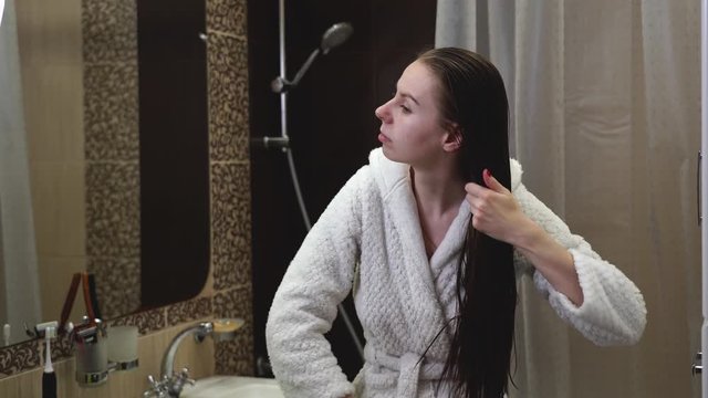 4K. Long shot. Girl / young woman combing wet hair after a shower. girl and comb. Girl combing her hair