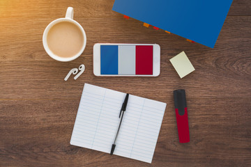 flag of France on a smartphone on a wooden table, notebook and pen, textbook, study concept 
