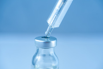 One medical glass bottle with red potion on a blue background and a medical disposable syringe with a needle. Medical concept shows a medical test tube and vaccines against coronavirus. Copy place