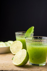 Top view of glasses with cucumber juice, cut limes, mint and cucumber slices, with selective focus, on wooden table, black background, vertical, with copy space