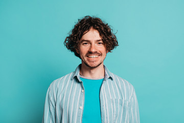 Cheerful happy guy isolated over blue background. Young man smiling on camera. Guy with long curly hair and beard posing alone in studio.