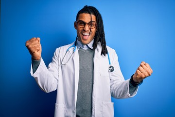 Young african american doctor man with dreadlocks wearing stethoscope and glasses celebrating surprised and amazed for success with arms raised and open eyes. Winner concept.