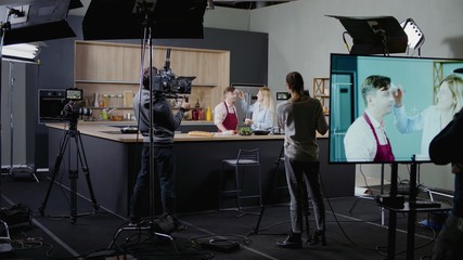 WIDE Behind the scenes of studio set, makeup artist make corrections during shooting television cooking show featuring celebrity chef, professional TV production