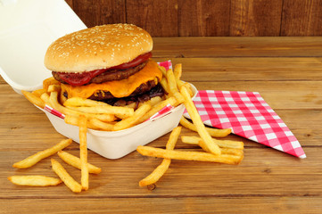 Double cheeseburger in a sesame seed covered bread bun with tomato sauce and French fries in a take...