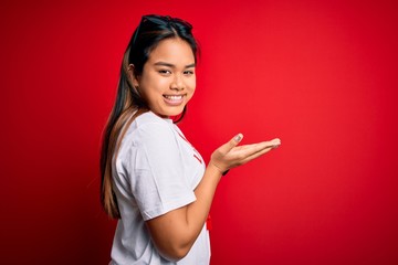 Young asian lifeguard girl wearing t-shirt with red cross using whistle over isolated background pointing aside with hands open palms showing copy space, presenting advertisement smiling excited happy