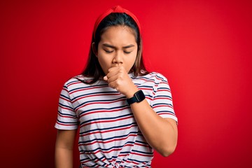 Young beautiful asian girl wearing casual striped t-shirt over isolated red background feeling unwell and coughing as symptom for cold or bronchitis. Health care concept.