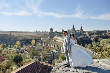 The bride and groom are walking near the old castle. The couple stands with their backs to each other.