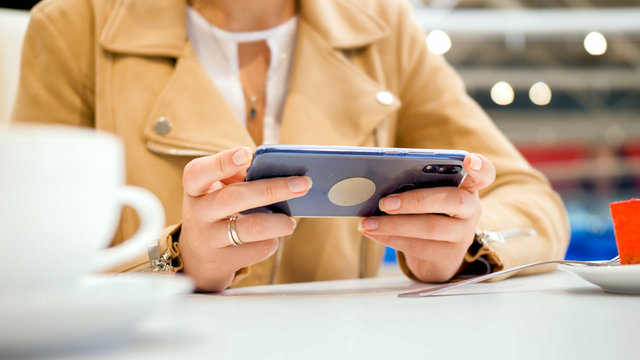 Closeup image of young woman sitting in cafe and holding smartphone in hands