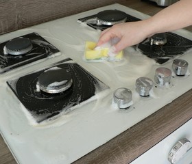 Cleaning dirty gas stove, foam from household chemicals. Hands hold a washing sponge in the foam....