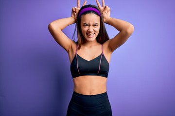 Obraz premium Young beautiful sporty girl doing sport wearing sportswear over isolated purple background Posing funny and crazy with fingers on head as bunny ears, smiling cheerful