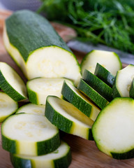 Chopping zucchini with a knife on a wooden board. 