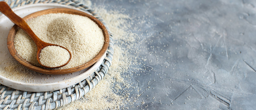 Raw uncooked fonio seeds with a spoon on a plate on grey background