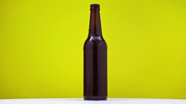 dark bottle of cold beer rotating on white surface isolated on lime green