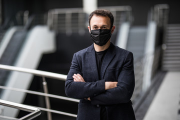 Businessman in medical mask works in an open space office. Male manager in a suit follows safety precautions during a coronavirus epidemic. Caring for the health of employees.