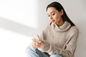 Image of smiling asian woman sitting and using smartphone