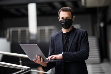 Protect yourself during a viral pandemic. Businessman in medical mask is standing with laptop in office