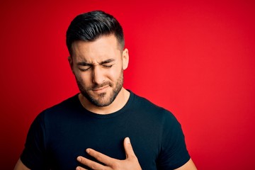 Young handsome man wearing casual black t-shirt standing over isolated red background with hand on stomach because indigestion, painful illness feeling unwell. Ache concept.