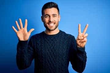 Young handsome man wearing casual sweater standing over isolated blue background showing and pointing up with fingers number seven while smiling confident and happy.