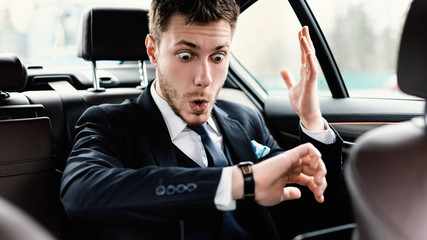 Stressed young businessman looking at wrist watch in car