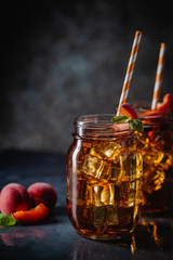 Glass of peach or apricot iced tea with fruit slices against dark blue background