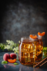 Glass of peach or apricot iced tea with fruit slices against dark blue background