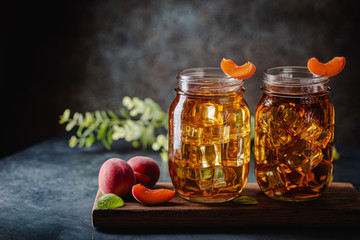 Glass of peach or apricot iced tea with fruit slices against dark blue background
