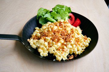 Bayrische Käsepätzle Kasspatzen mit Röstzwiebeln in einer Eisenpfanne auf einem Holztisch