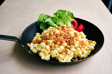 Bayrische Käsepätzle Kasspatzen mit Röstzwiebeln in einer Eisenpfanne auf einem Holztisch
