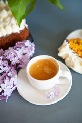 Fresh espresso in a white cup and lilac flowers on the background.