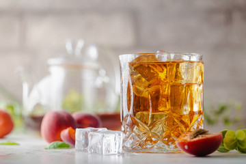 Glass of peach or apricot iced tea with fruit slices against white background