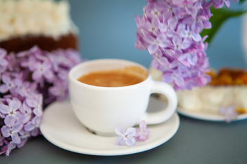 Obraz na płótnie Canvas Fresh espresso in a white cup and lilac flowers on the background.
