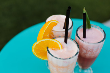 three colorful smoothie drinks on a blue table on a terrace, summer time
