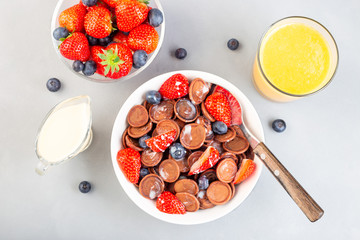 Trendy small chocolate cereal pancakes served with condensed milk, strawberry, blueberry and orange juice, in white bowl, horizontal, top view