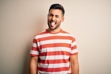 Young handsome man wearing casual striped t-shirt standing over isolated white background sticking tongue out happy with funny expression. Emotion concept.