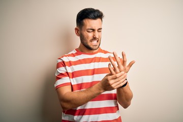 Fototapeta premium Young handsome man wearing casual striped t-shirt standing over isolated white background Suffering pain on hands and fingers, arthritis inflammation