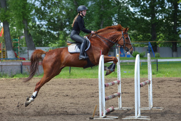 Girl in equestrian uniform on horseback jumping hurdle obstacle 