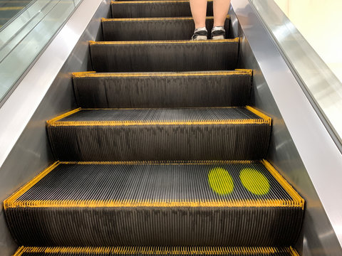 Woman standing on escalator with color mask on stair for social distancing.