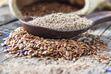 Crushed flax seed in a wooden spoon on a pile of flaxseed.