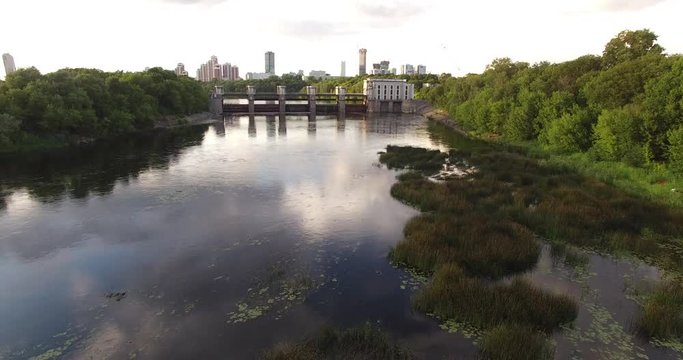 4K cloudy afternoon aerial scenic footage of Mnevniki hydro system dam regulating Moscow River water levels overlooking green park, distant city sky scrapers in Krylatskoye area in Moscow, Russia