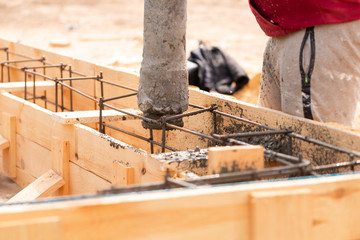 Close up of construction worker laying cement or concrete into the foundation formwork with automatic pump