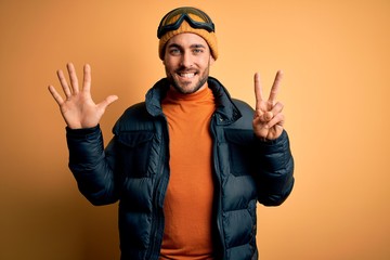 Young handsome skier man with beard wearing snow sportswear and ski goggles showing and pointing up with fingers number seven while smiling confident and happy.