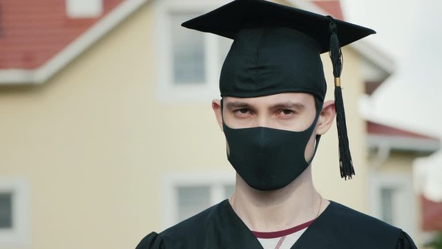 Portrait of a graduate in a protective mask, wearing a robe and a graduate cap