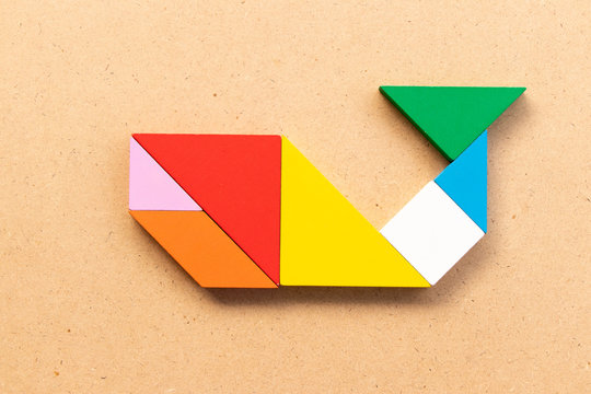Color tangram puzzle in whale, fish or shark shape on wood bacground