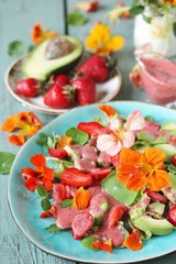 salad with nasturtium flowers and leaves with strawberries and avocados. dressed with strawberry vinaigrette or strawberry dressing with poppy seeds. bright summer salad with edible flowers. 
