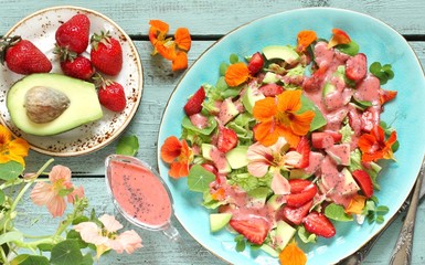 salad with nasturtium flowers and leaves with strawberries and avocados. dressed with strawberry vinaigrette or strawberry dressing with poppy seeds.