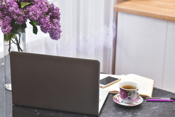 Grey leptop with cup of tea, flowers on the clear vase at the black table