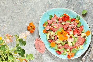 salad with nasturtium flowers and leaves with strawberries and avocados. dressed with strawberry vinaigrette or strawberry dressing with poppy seeds. edible flowers. top view, copy space