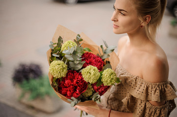 young woman holds stylish bouquet of red peonies with green hydrangea with eucalyptus leaves.