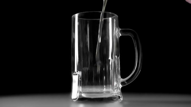 slow motion of light beer flowing into empty mug isolated in black
